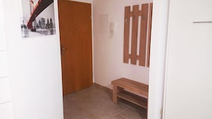 Un couloir avec une porte en bois, un banc, un téléphone fixé au mur et une affiche représentant un paysage urbain.