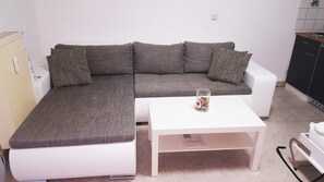 A modern living room with a grey sofa, white coffee table, and a small kitchen area. - KaRest – Compact Apartment with Balcony (Neckarsulm)