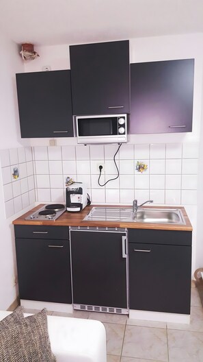A compact kitchen with a microwave, toaster, sink, and cabinets. - KaRest – Compact Apartment with Balcony (Neckarsulm)