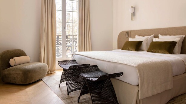 A bedroom with a large bed, a chair, a small table, and a window with curtains. - Harmony Collection I 2BR Suite 4P AC Opera Grevin (Paris)