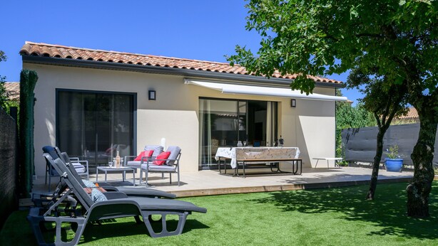 Un patio extérieur moderne, doté de chaises longues, d’une table et d’un espace salon abrité.