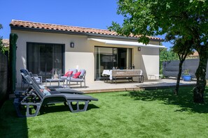 Un patio extérieur moderne, doté de chaises longues, d’une table et d’un espace salon abrité.