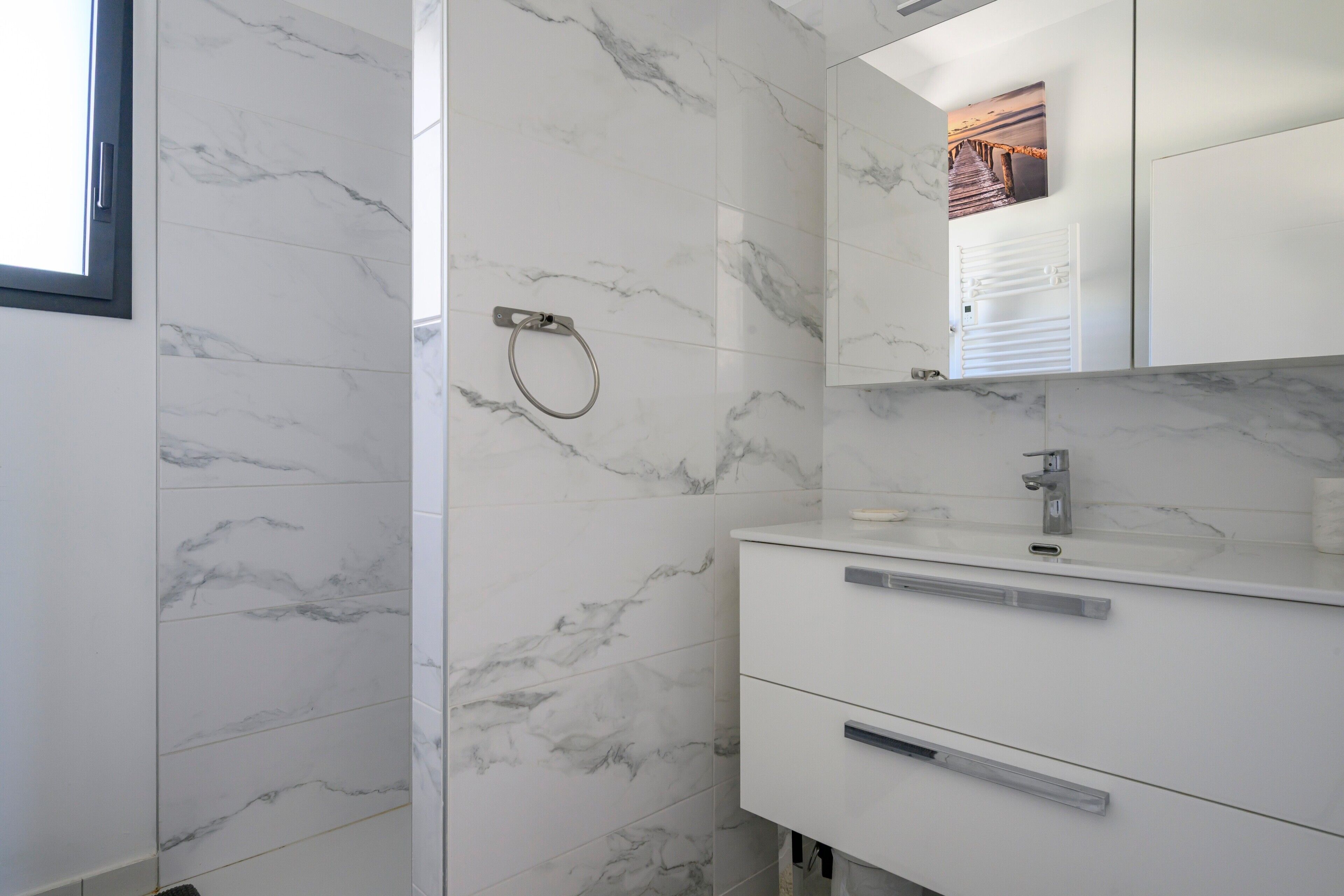 Un bagno con piastrelle in marmo bianco, un porta asciugamani, uno specchio e un lavandino moderno.