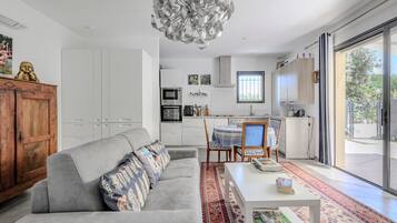 Ein stilvoller Wohnbereich mit grauem Sofa, einem Esstisch und einer Küchenzeile mit weißen Schränken und einem eingebauten Backofen.