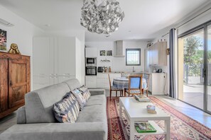 Een moderne woonruimte met een grijze bank, een eettafel en een keuken met witte kasten en een ingebouwde oven.