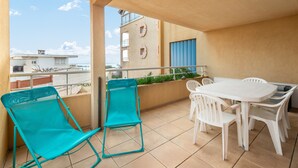 A balcony with a white table and chairs, two turquoise chairs, and a view of buildings and the sea. - apartment with sea view, sleeps 6, balcony (Valras-Plage)