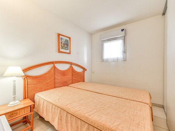 A bedroom with a bed, a bedside table, a lamp, a window with an air conditioner, and a framed picture on the wall. - apartment with sea view, sleeps 6, balcony (Valras-Plage)