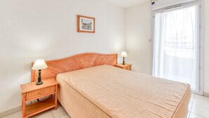 A bedroom with a large bed, two bedside tables with lamps, a framed picture on the wall, and a sliding glass door to the right. - apartment with sea view, sleeps 6, balcony (Valras-Plage)