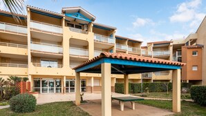 A multi-story building with balconies, a covered seating area, and a well-maintained lawn. - apartment with sea view, sleeps 6, balcony (Valras-Plage)