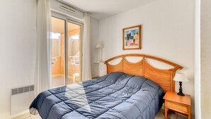 Ein Schlafzimmer mit einem Bett, einem Nachttisch, einer Lampe, einem Gemälde und einer Schiebetür, die auf einen Balkon führt.