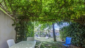 Eine Außenpatio mit Tisch und Stühlen, umgeben von Grünpflanzen und Blick auf ein Haus im Hintergrund.