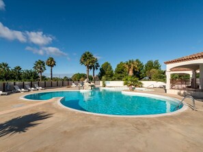 Une piscine avec des chaises longues, des palmiers et un bâtiment doté d’un toit en tuiles.