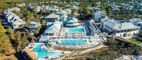 An aerial view of a resort with a large pool, multiple buildings, and surrounding greenery.