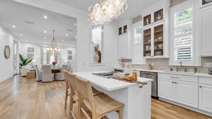 Una cocina moderna con armarios blancos, una isla central y un comedor con candelabro.