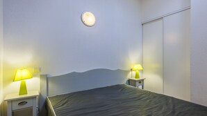 Une chambre à coucher comprenant un lit, deux tables de chevet avec des lampes, un luminaire fixé au mur et une armoire.