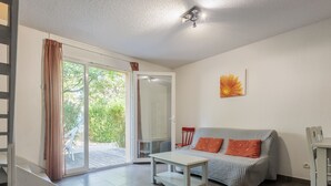 Un salon comprenant un canapé, une petite table, un fauteuil et une porte-fenêtre coulissante donnant sur un balcon.