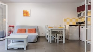Un espace de vie compact comprenant un coin cuisine, un coin repas et un canapé avec des coussins orange.