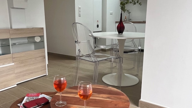 Una sala de estar moderna con una mesa de centro de madera, dos sillas transparentes y un jarrón rojo con una planta.