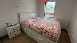 Un dormitorio con una cama, una mesita de noche, un ventanal y una lámpara colgante roja.