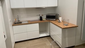 Cocina compacta con armarios blancos, encimera de madera, microondas, hervidor y un lavamanos pequeño.