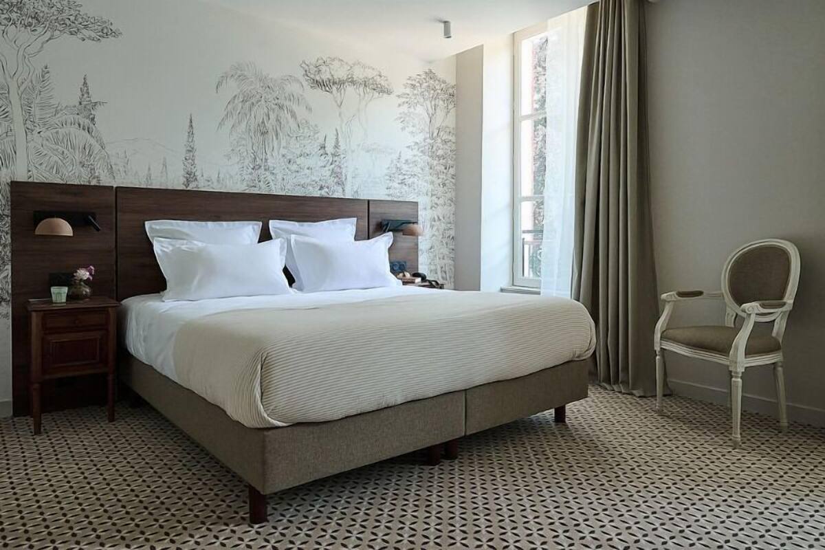 A neatly made bed with white linens, a wooden headboard, a small bedside table with a lamp, and a chair.