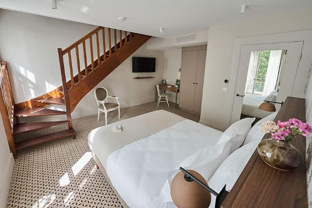 A bedroom with a bed, a wooden staircase, a desk, and a chair.