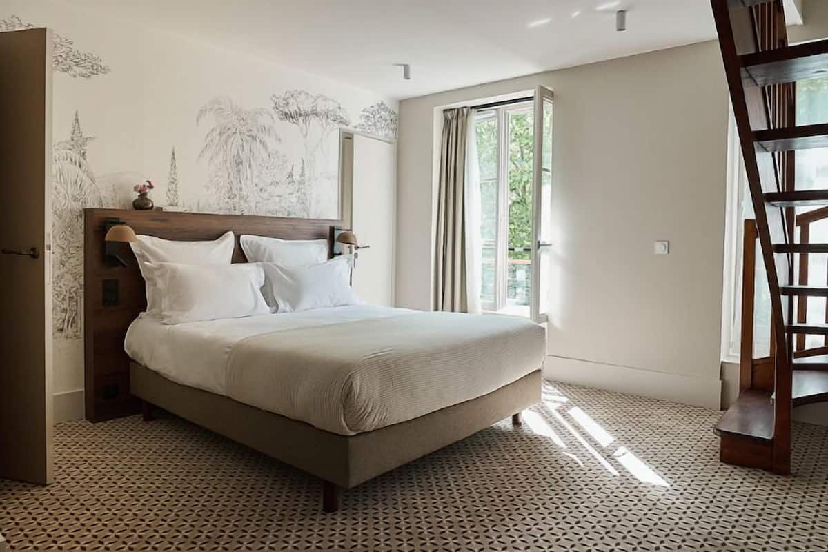A bedroom with a bed, a wooden headboard, a window with curtains, and a staircase.
