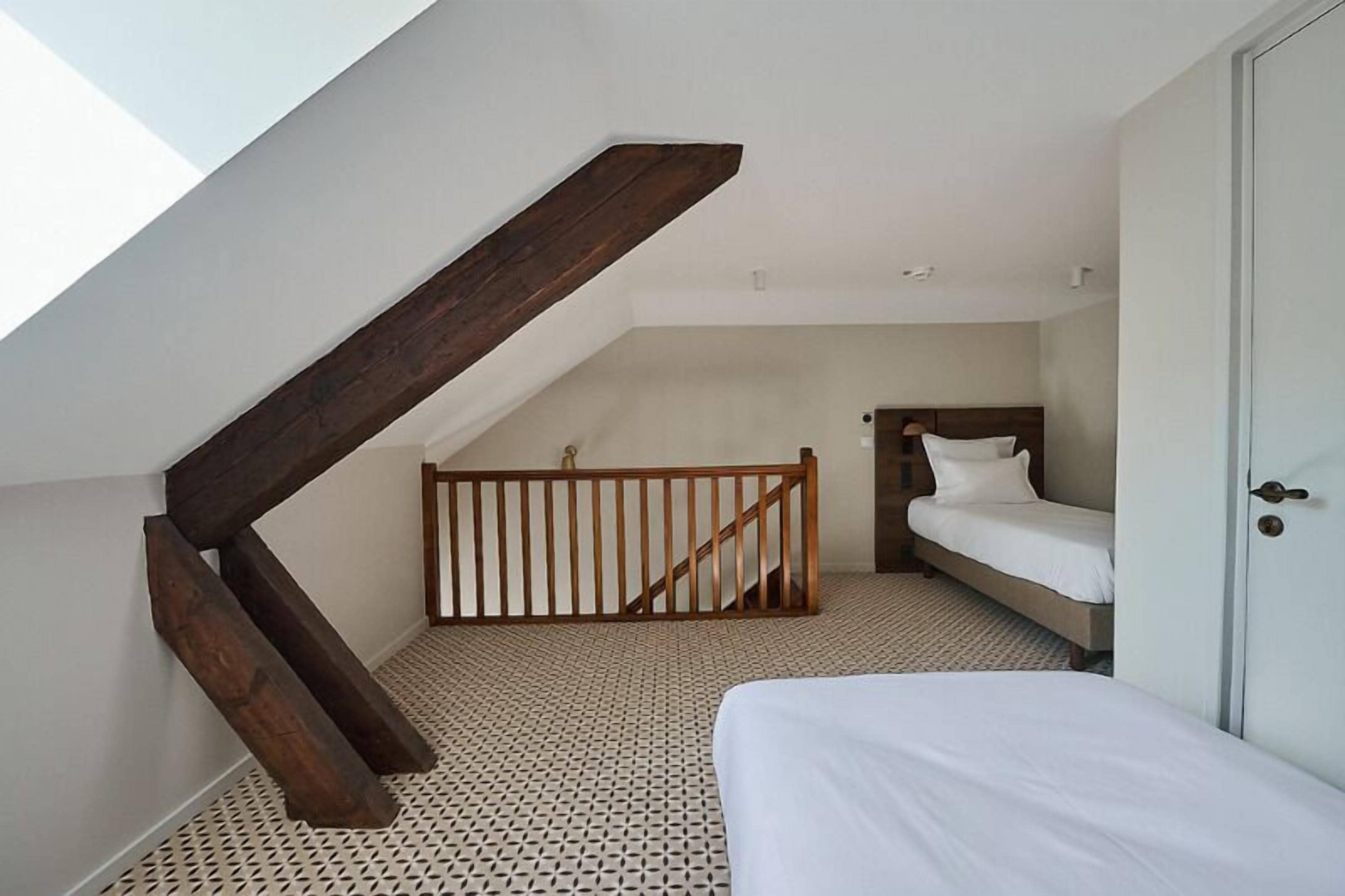 A bedroom with a sloped ceiling, a wooden staircase, a bed, and a door.