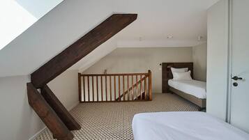 A bedroom with a sloped ceiling, a wooden staircase, a bed, and a door.