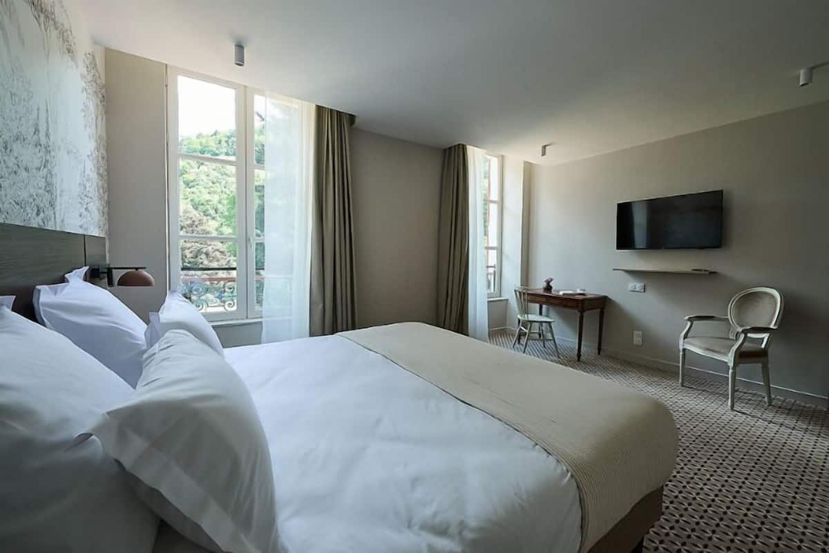 A hotel room with a large bed, a desk, a chair, a TV, and a window with curtains.