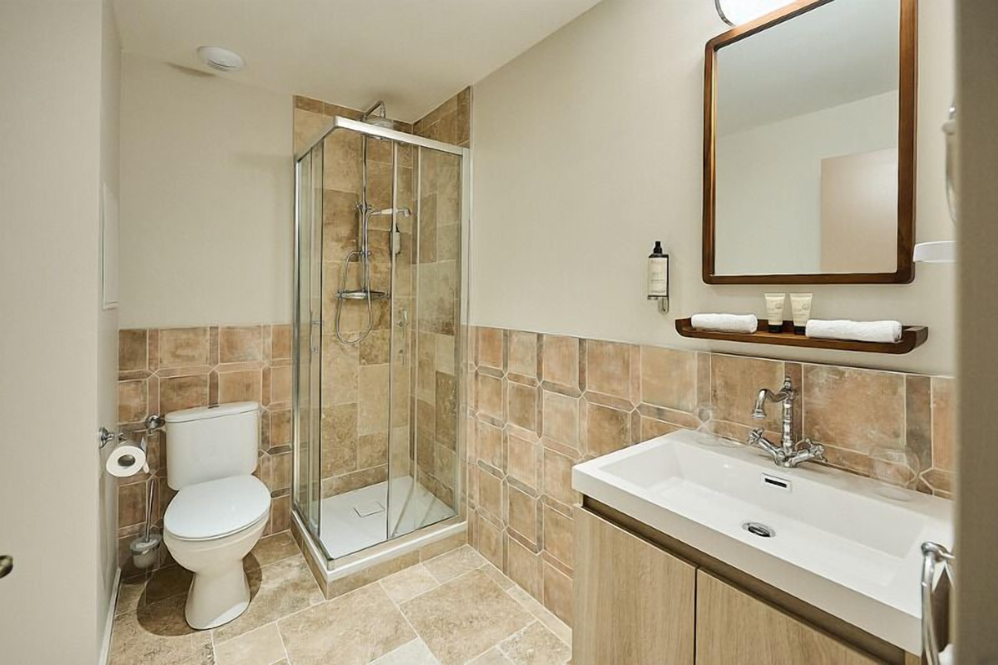 Un baño con cabina de ducha de vidrio, un inodoro, un lavamanos y un espejo.