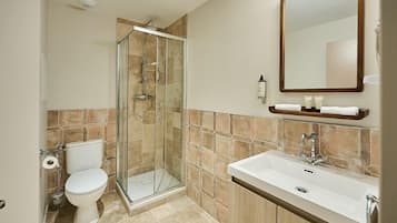 Un baño con cabina de ducha de vidrio, un inodoro, un lavamanos y un espejo.