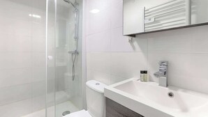 A modern bathroom with a glass-enclosed shower, a white sink, and a mirror above the sink. - Studio de charme au cœur du Sentier (Paris)