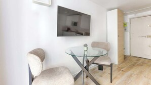 A modern room with a glass-top table and two chairs, a white door, and a framed picture on the wall. - Studio de charme au cœur du Sentier (Paris)