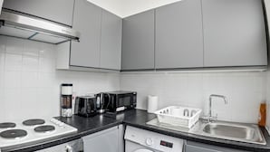 A modern kitchen with grey cabinets, a built-in stove, a microwave, a toaster, and a dishwasher. - Charming Studio in Harborne (Birmingham)