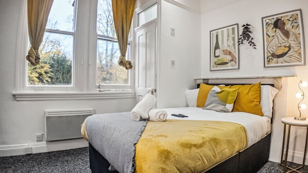 A hotel room with a bed, a bedside table with a lamp, and two framed pictures on the wall. - Charming Studio in Harborne (Birmingham)