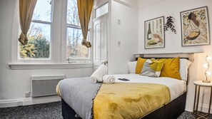 A hotel room with a bed, a bedside table with a lamp, and two framed pictures on the wall. - Charming Studio in Harborne (Birmingham)