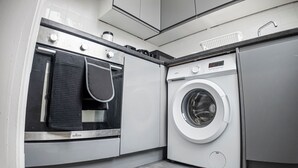 A modern laundry room with a washing machine, a dryer, and a built-in oven. - Charming Studio in Harborne (Birmingham)