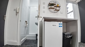 A compact hotel room with a kitchenette, a small bathroom, and a view of the outside. - Charming Studio in Harborne (Birmingham)