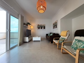 Uma sala de estar moderna com televisão, sofá, poltrona, porta de varanda e luminária de teto.