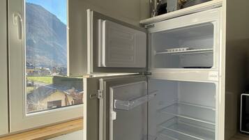 A kitchen with a built-in refrigerator, a window with a view of a mountain, and a shelf with kitchen utensils.