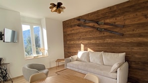 A modern living room with a wooden wall, a white sofa, a wooden dining table, and a decorative snowflake.