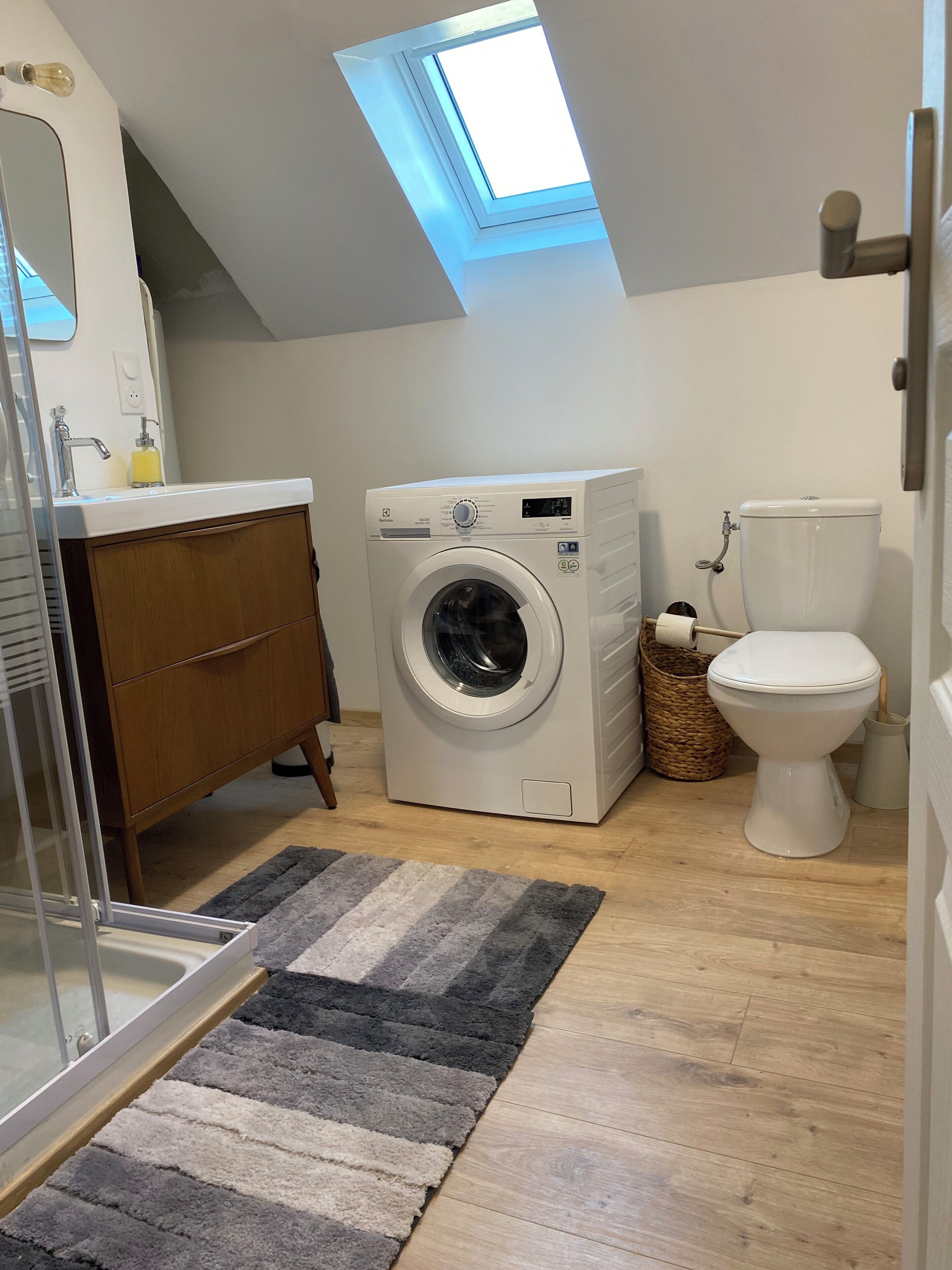 A compact laundry room with a washing machine, a toilet, and a skylight.