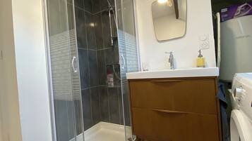 Une salle de bain moderne dotée d’une douche à parois de verre, d’un meuble-lavabo en bois et d’un lave-linge encastré.