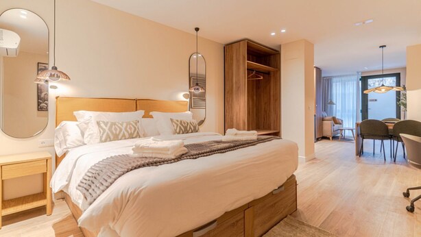 Un dormitorio moderno con una cama grande, cabecero de madera, mesitas de noche, un armario y una zona de comedor con sillas y una mesa.