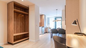 Una habitación moderna con un armario de madera, una zona de comedor con una mesa y sillas, y una lámpara colgante.