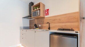 Una cocina moderna con microondas integrado, un fregadero y lavavajillas. Hay una estantería de madera sobre el microondas y un letrero rojo de extintor en la pared.
