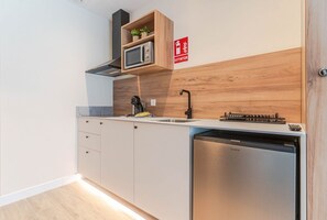 Eine moderne Küche mit integriertem Mikrowellenherd, Spüle und Geschirrspüler. Oberhalb des Mikrowellenherds befindet sich ein Holzregal und an der Wand ist ein rotes Schild für Feuerlöscher angebracht.