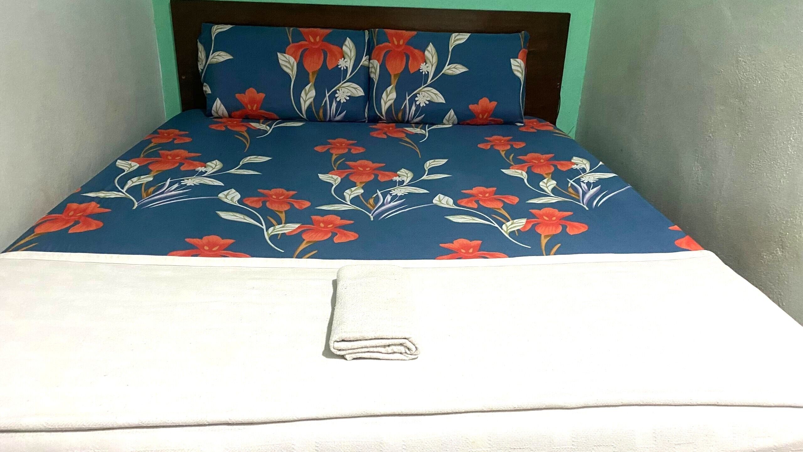 A bed with a blue floral bedspread and a white blanket.