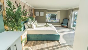 A bedroom with a large bed, a view of the outdoors, a chair, and a window.